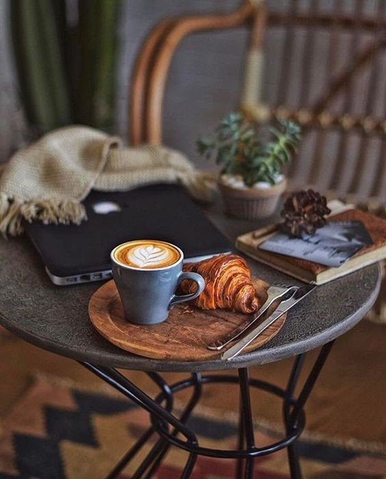 یک فنجان قهوه و کروسانت روی سینی چوبی روی میز کافه