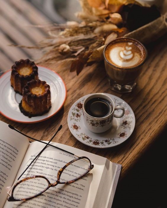 یک فنجان قهوه و کتاب و شیرینی روی میز چوبی