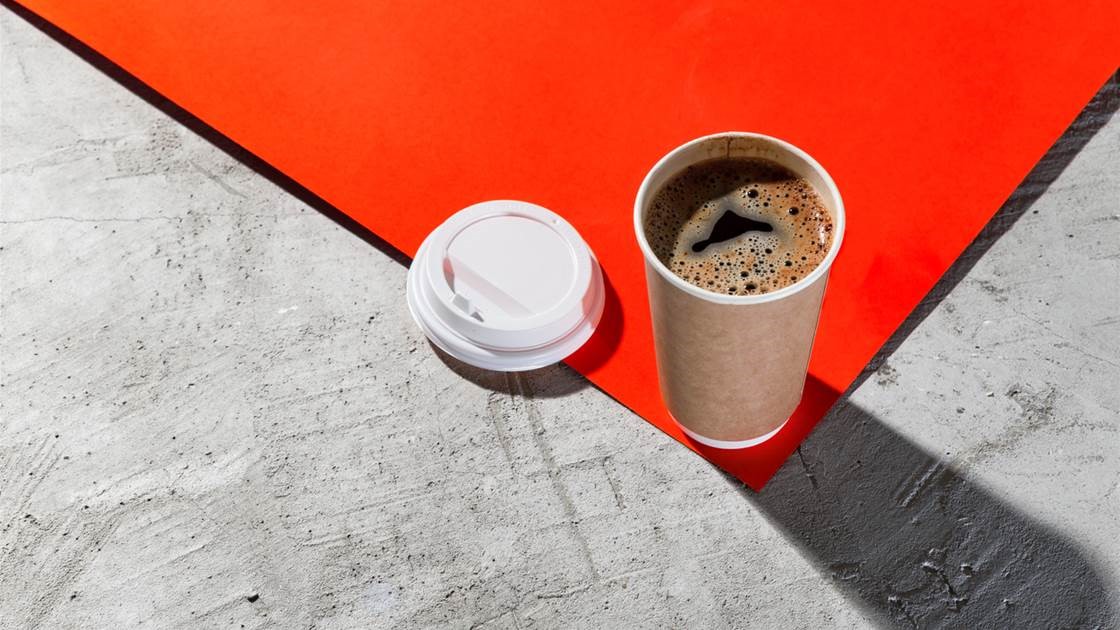 لیوان قهوه یکبار مصرف روی سطح بتنی و کاغذ نارنجی